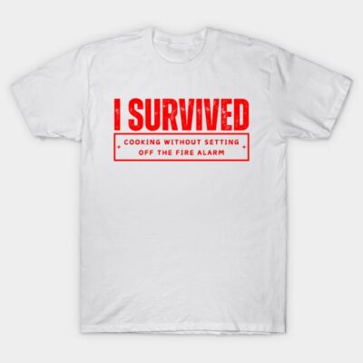 White cotton T-shirt with red text "I Survived Cooking Without Setting Off the Fire Alarm," casual humorous apparel.