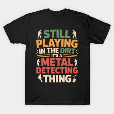 Black t-shirt with colorful text design "Still Playing in the Dirt It's a Metal Detecting Thing," casual and fun style.