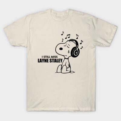 Cream t-shirt featuring cartoon dog with headphones, musical notes, and "I Still Miss Layne Staley" text, casual wear.