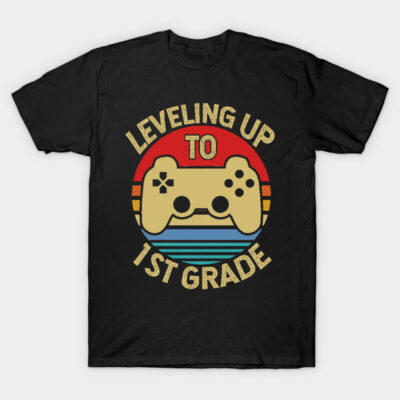 Black t-shirt with "Leveling Up to 1st Grade" and game controller graphic in retro colors, perfect for kids.