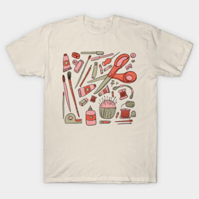 Beige t-shirt with colorful art supplies design, featuring scissors, paintbrushes, and yarn, perfect for artists.