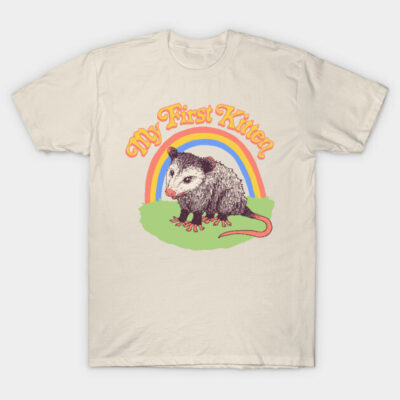 Cream t-shirt with a playful opossum design, colorful rainbow background, text "My First Kitten", casual style.