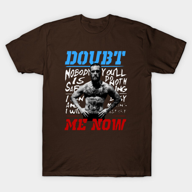 Brown graphic t-shirt with bold "Doubt Me Now" text in blue and red, featuring a monochrome design for casual wear.