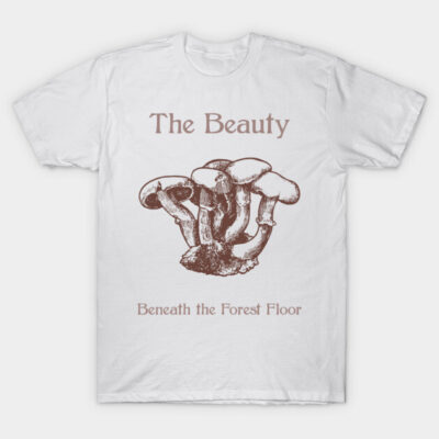 White t-shirt with brown mushroom illustration and text, "The Beauty Beneath the Forest Floor," casual style, cotton material.