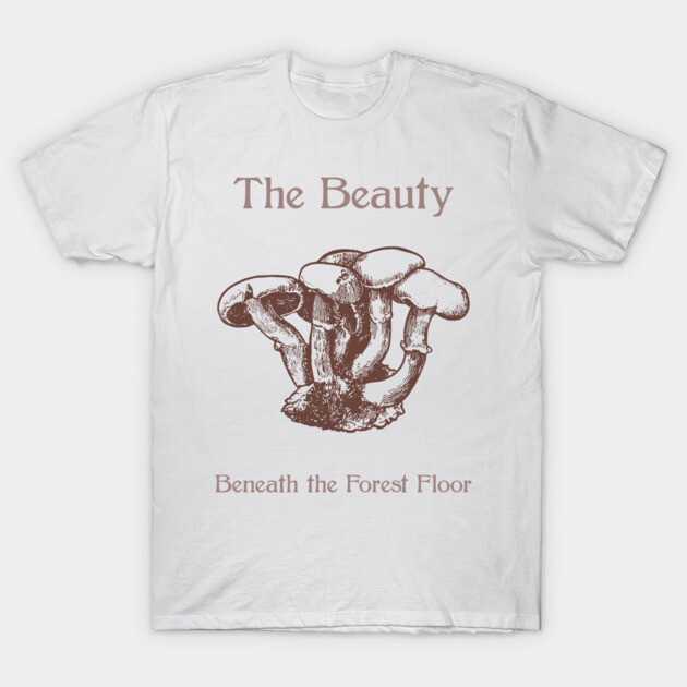 White t-shirt with brown mushroom illustration and text, "The Beauty Beneath the Forest Floor," casual style, cotton material.