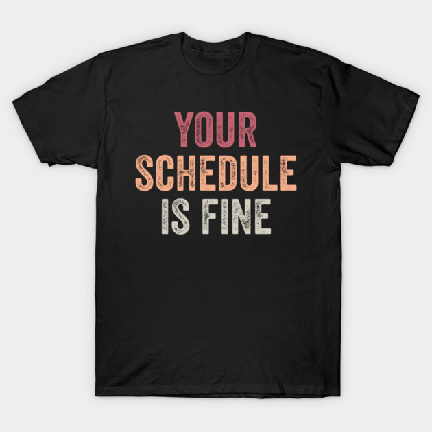 Black cotton T-shirt with "Your Schedule is Fine" text in red, orange, and white. Casual wear, unisex style.