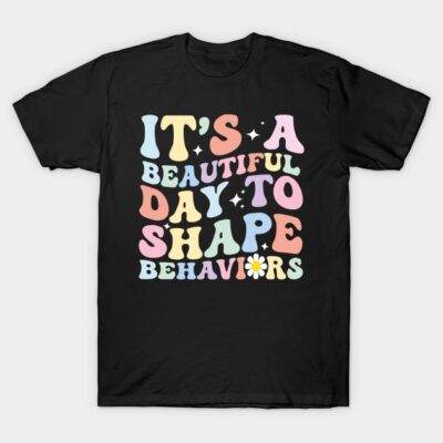 Black t-shirt with colorful retro text design, "It's a Beautiful Day to Shape Behaviors," casual wear, cotton fabric.