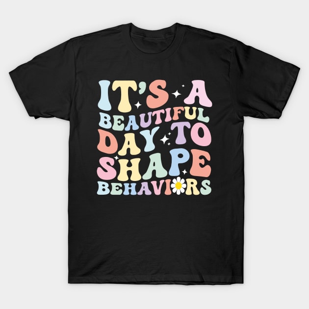 Black t-shirt with colorful retro text design, "It's a Beautiful Day to Shape Behaviors," casual wear, cotton fabric.