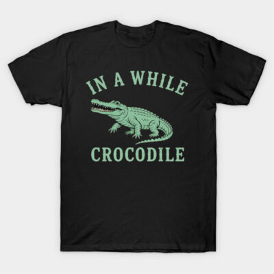 Black graphic T-shirt featuring green crocodile illustration and "In a While Crocodile" text, casual cotton wear.