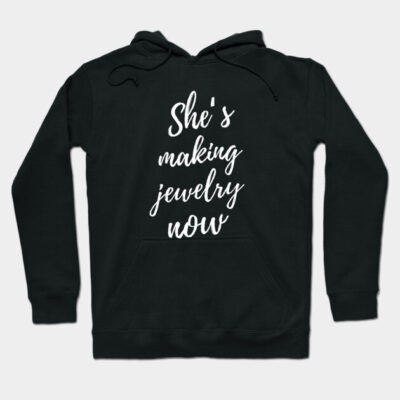 Black hoodie with "She's making jewelry now" text, casual style, cozy cotton material, perfect for everyday wear.