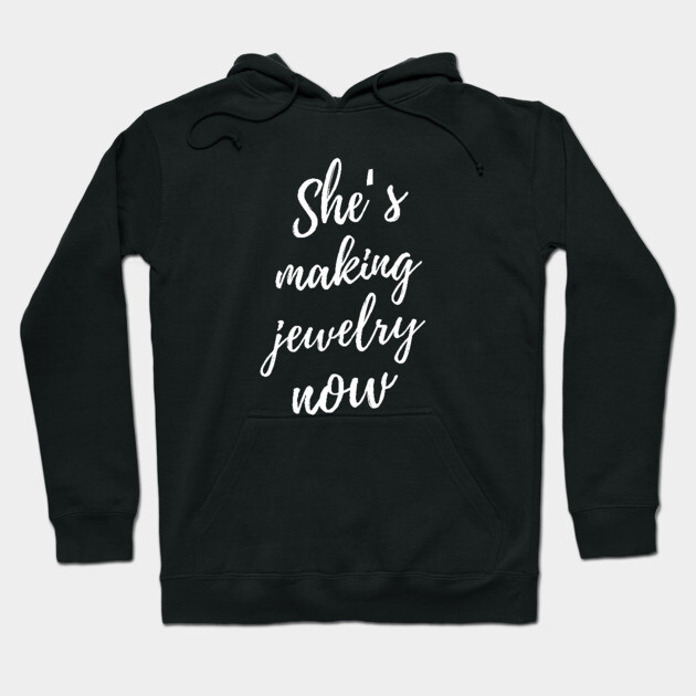 Black hoodie with "She's making jewelry now" text, casual style, cozy cotton material, perfect for everyday wear.
